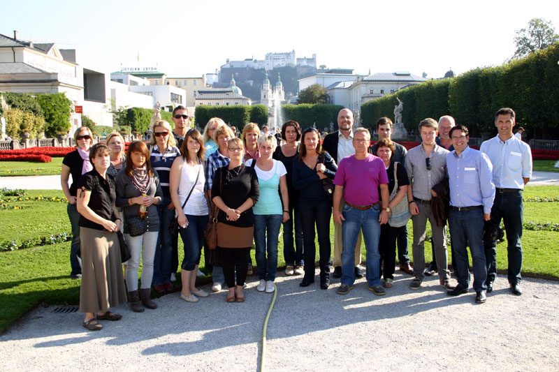 Gruppenfoto des AMOS-Teams im Mirabellgarten in Salzburg, im Hintergrund die Festung Hohensalzburg