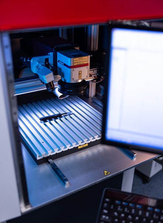 Blick in eine Laseranlage: Laserkopf über dem Arbeitstisch, daneben ein Bildschirm